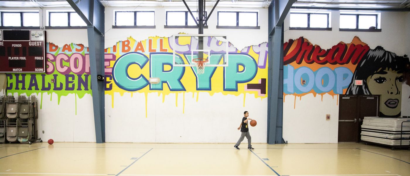 Boy bouncing basketball in a gym with colorful, expressive graffiti on walls