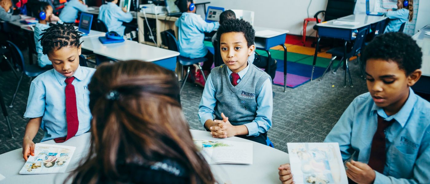 Boys in Prodeo Academy uniforms actively engaged by a teacher around a circular table